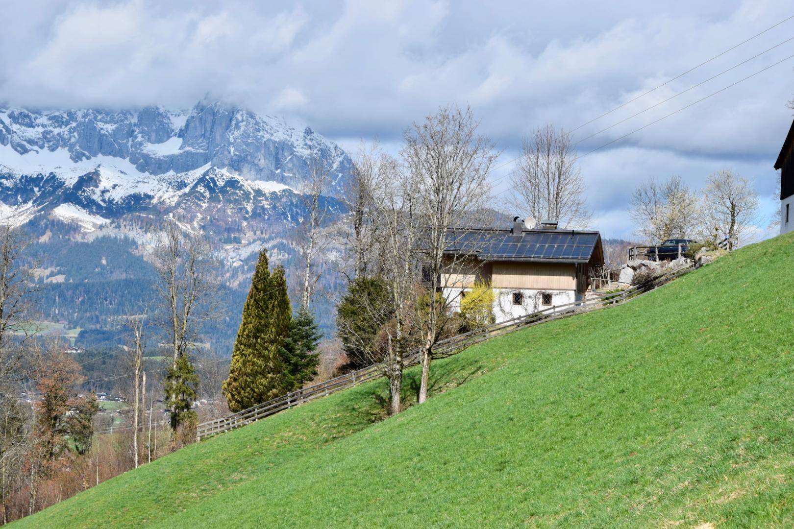 Haus auf einem steilen grünen Hang mit beeindruckendem Blick auf die schneebedeckten Berge.