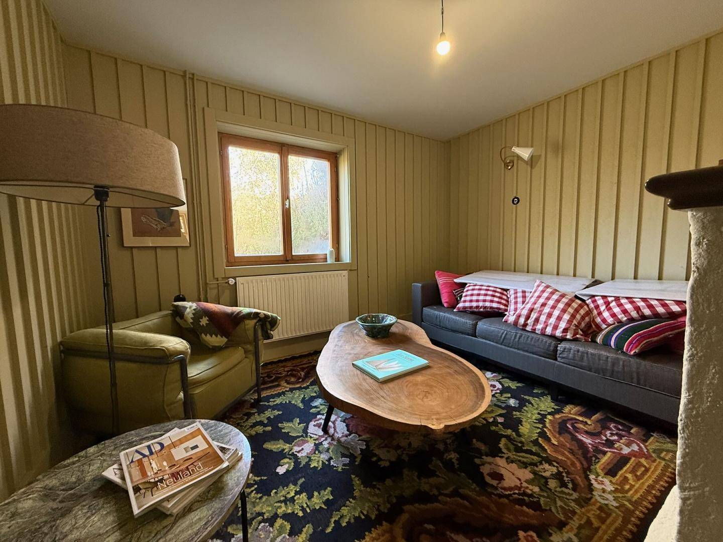 Gemütliches Wohnzimmer mit Holzvertäfelung, bequemen Möbeln und Blick ins Grüne.