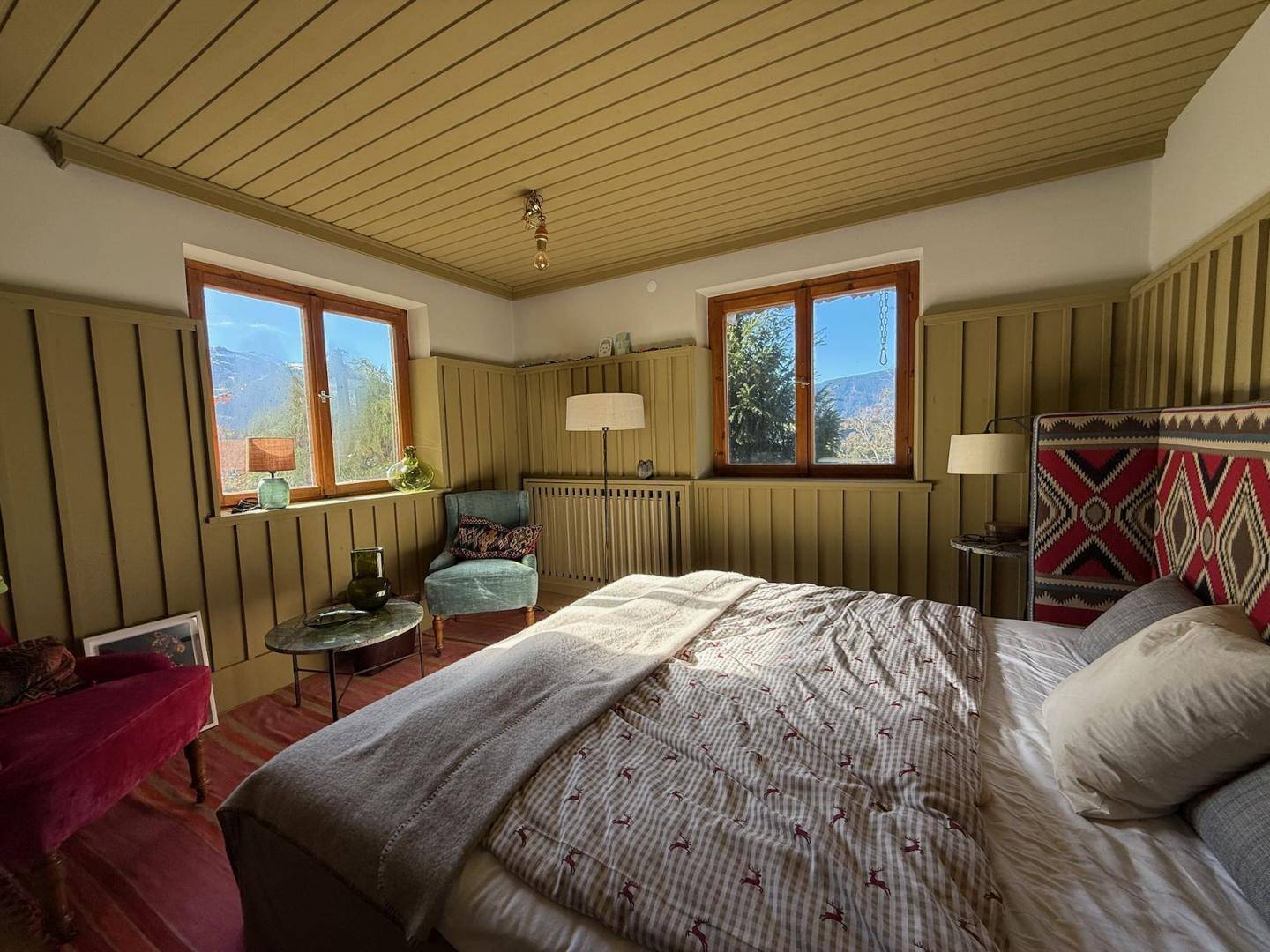 Helles Schlafzimmer mit Holzwänden, gemütlichem Bett und weitem Blick auf die Berge.