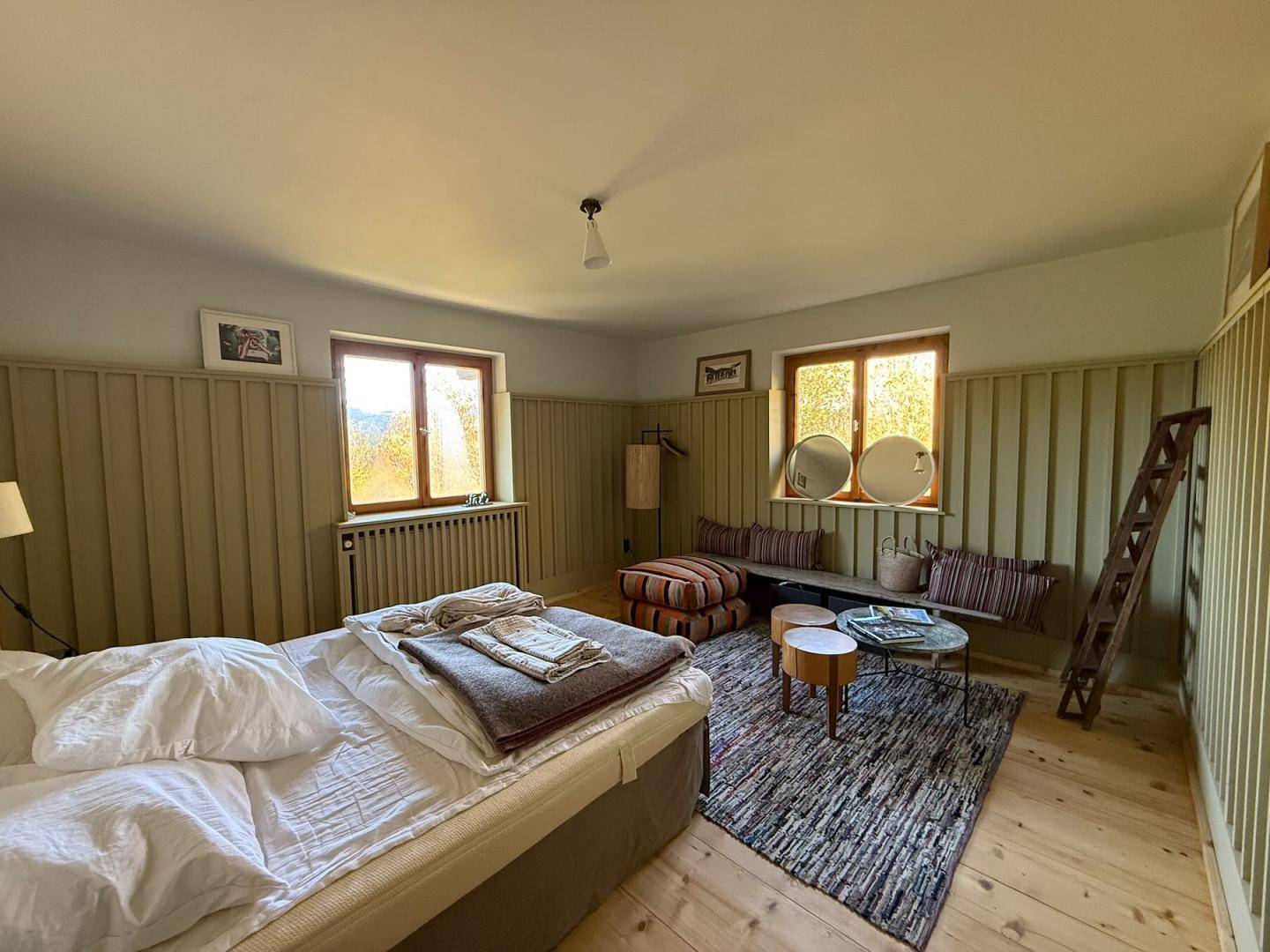 Lichtdurchflutetes Schlafzimmer mit Holzboden, Sitzbereich und Blick in die Natur.