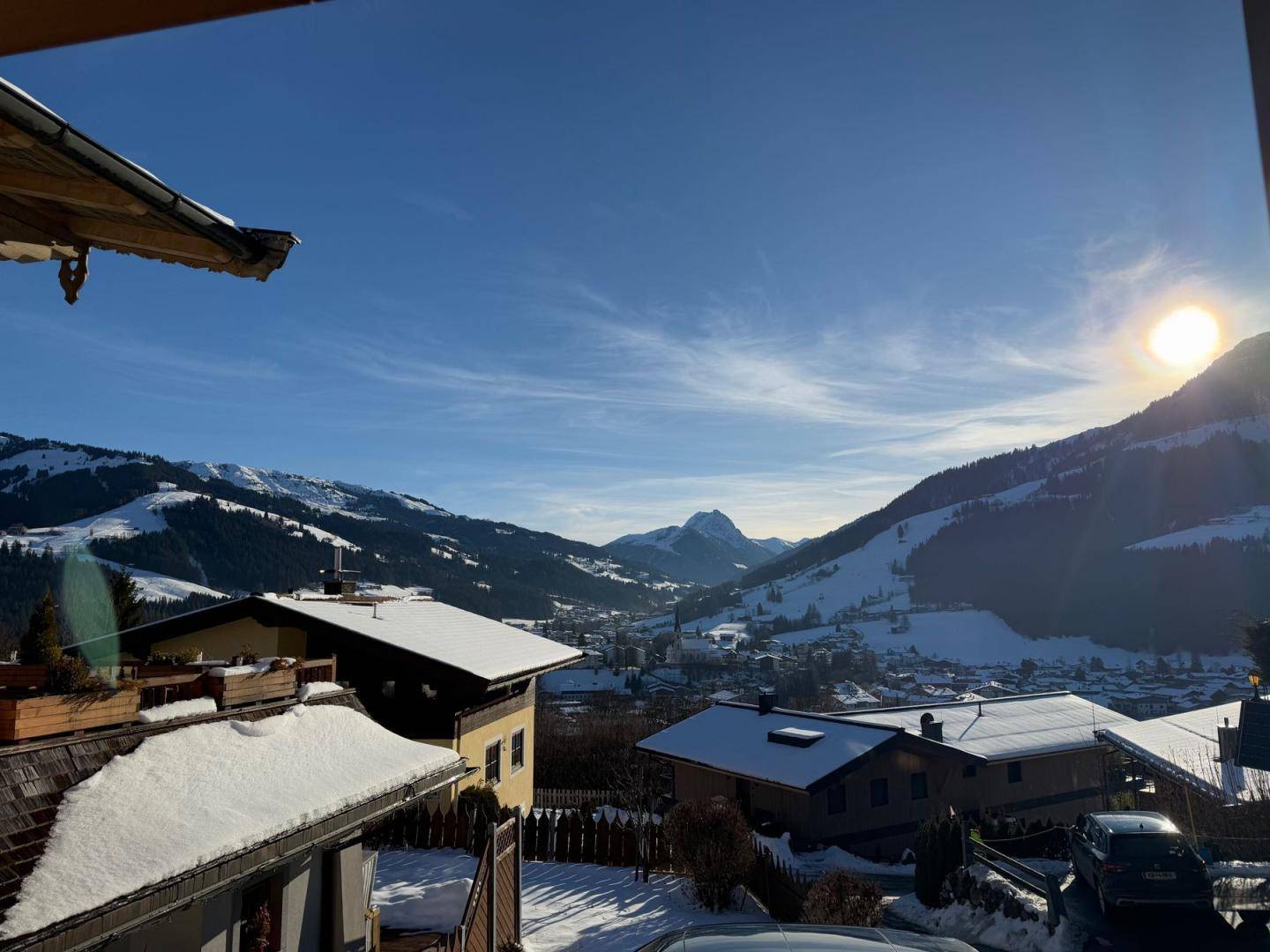 Panoramablick auf die verschneite Berglandschaft und die umliegenden Häuser unter blauem Himmel.