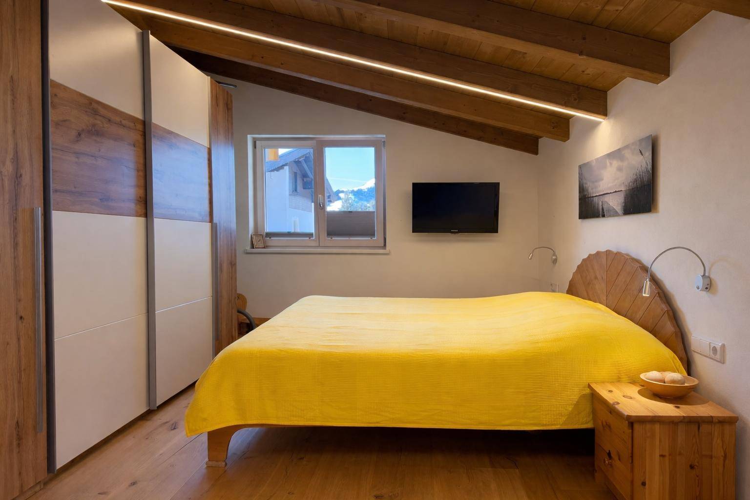 Schlafzimmer mit Holzbalkendecke, Holzboden und praktischen Einbauschränken unter der Dachschräge.