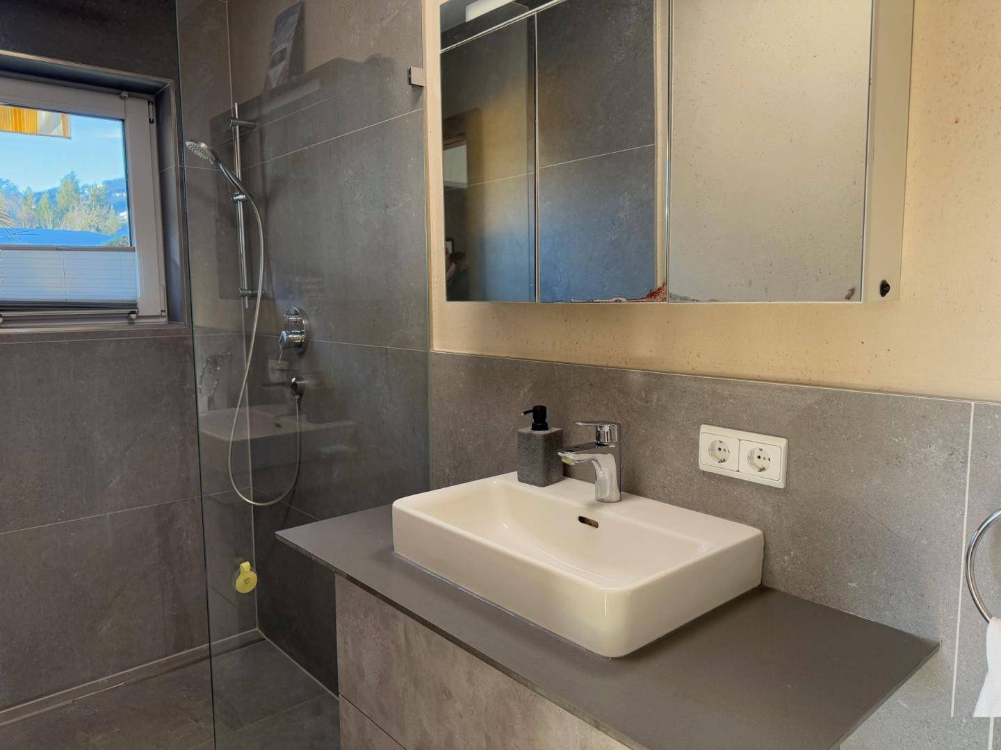 Zeitgemäßes Badezimmer mit großformatigen grauen Fliesen, Einzelwaschbecken und Spiegelschrank.