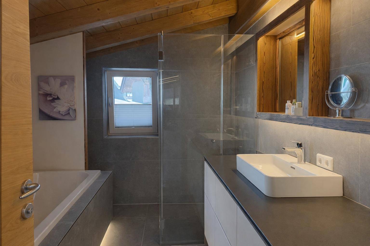 Modernes Badezimmer mit grauen Fliesen, begehbarer Dusche und Badewanne unter der Dachschräge.