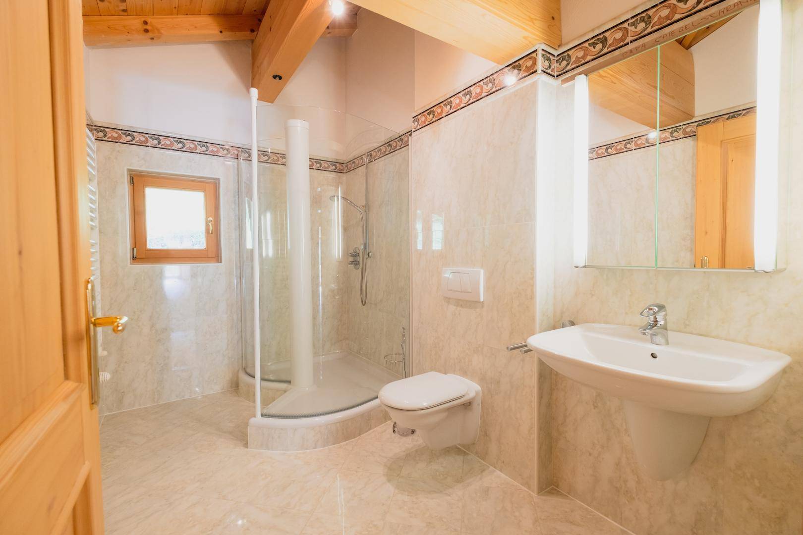 Modernes Badezimmer mit Fliesen, Holzbalkendecke, Duschkabine, WC und Spiegelschrank.