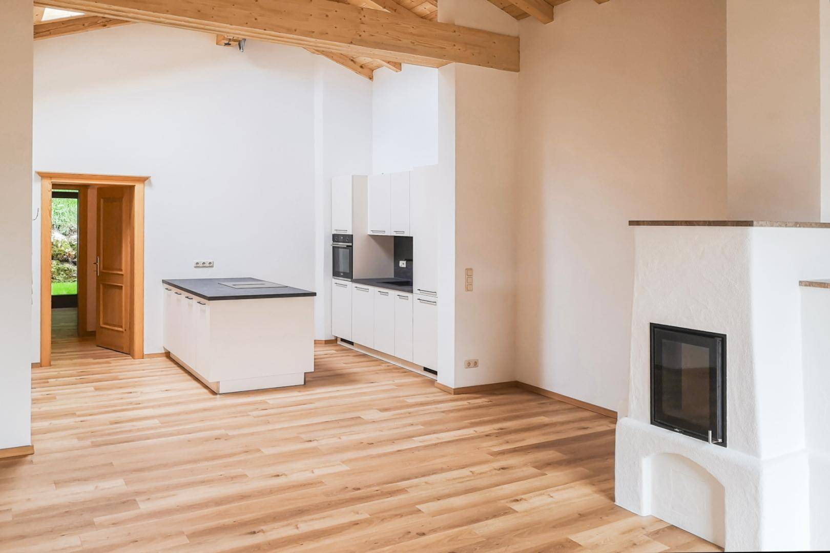 Geräumiger Wohn-Essbereich mit integrierter Küche, Kamin und Holzbalken an der Decke.