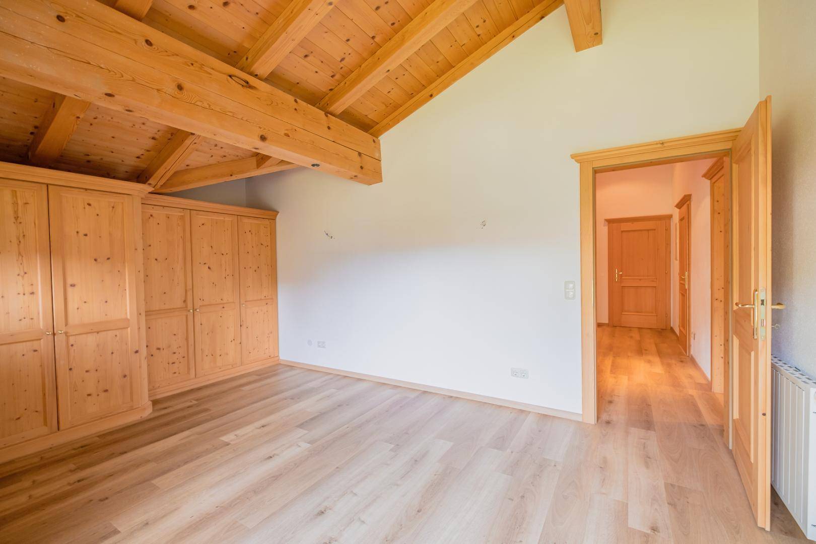 Helles Schlafzimmer mit Holzbalkendecke, integrierten Holzschränken und Zugang zum Flur.