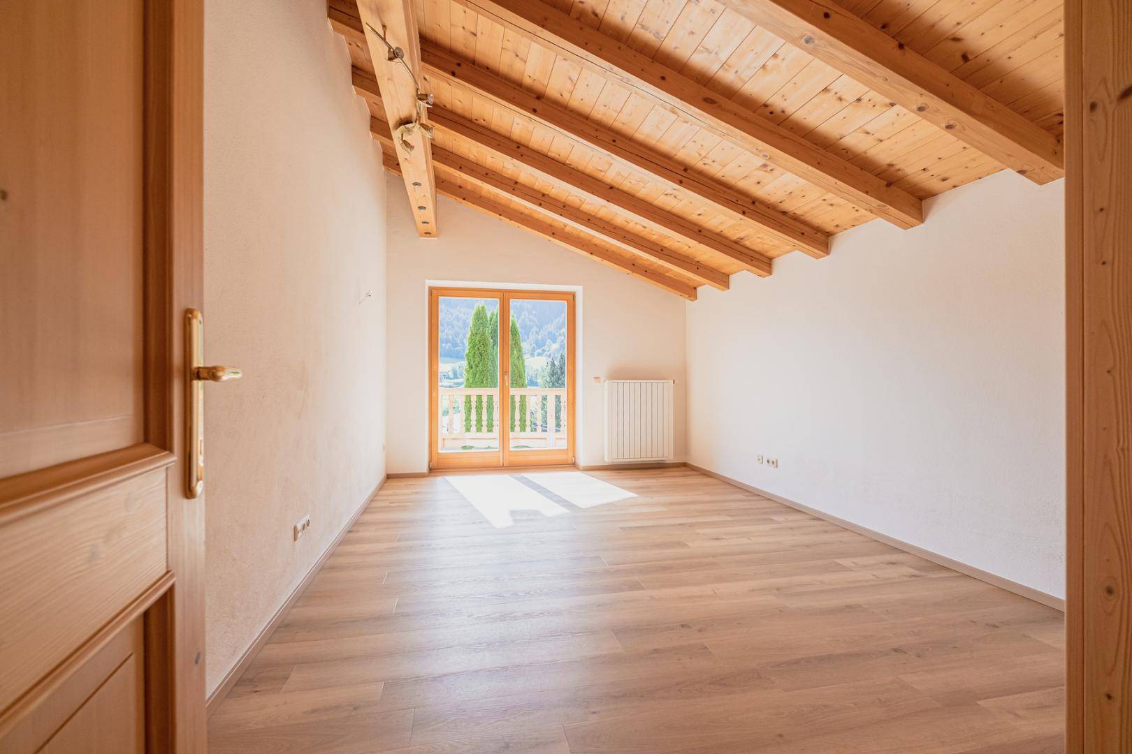 Schlafzimmer mit Holzbalkendecke, Parkettboden und Balkonzugang mit Bergblick.