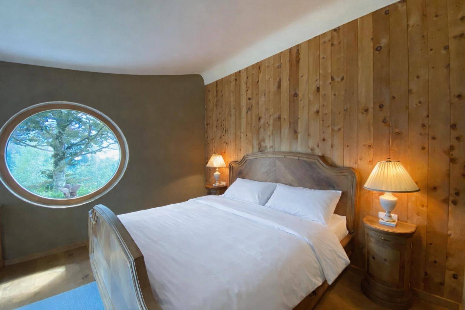 Schlafzimmer mit Holzwand, Rundfenster und Blick in die Natur.