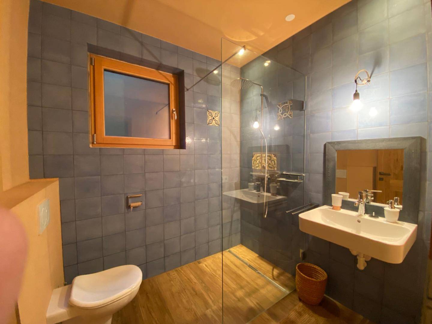 Modernes Badezimmer mit blauen Fliesen, Dusche, Fenster und Einzelwaschbecken.