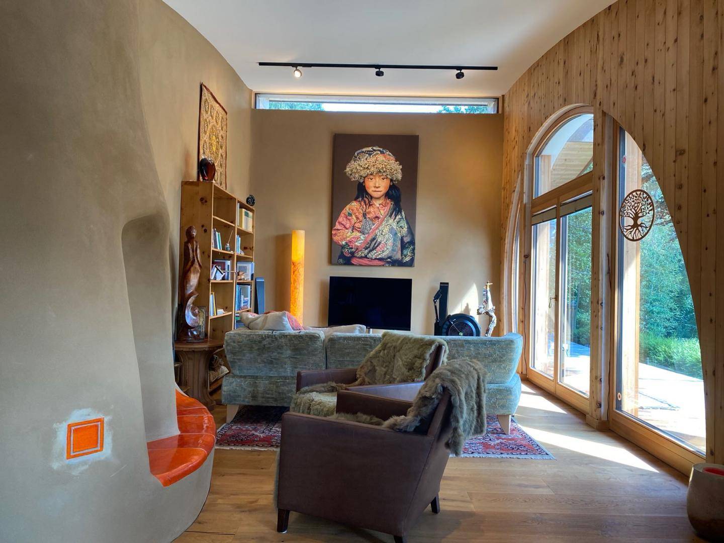 Helles Wohnzimmer mit Holzboden, Erdwänden, großen Fenstern und moderner Kunst.