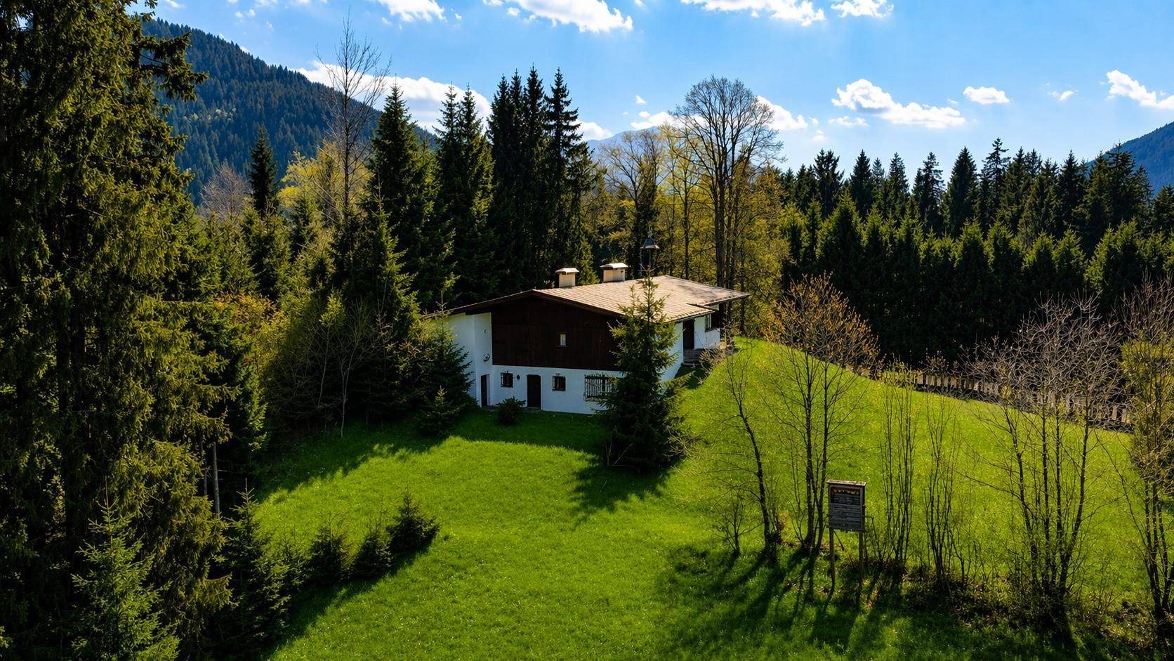 Haus in idyllischer Lage, umgeben von dichtem Wald und grünen Hügeln mit Bergblick.