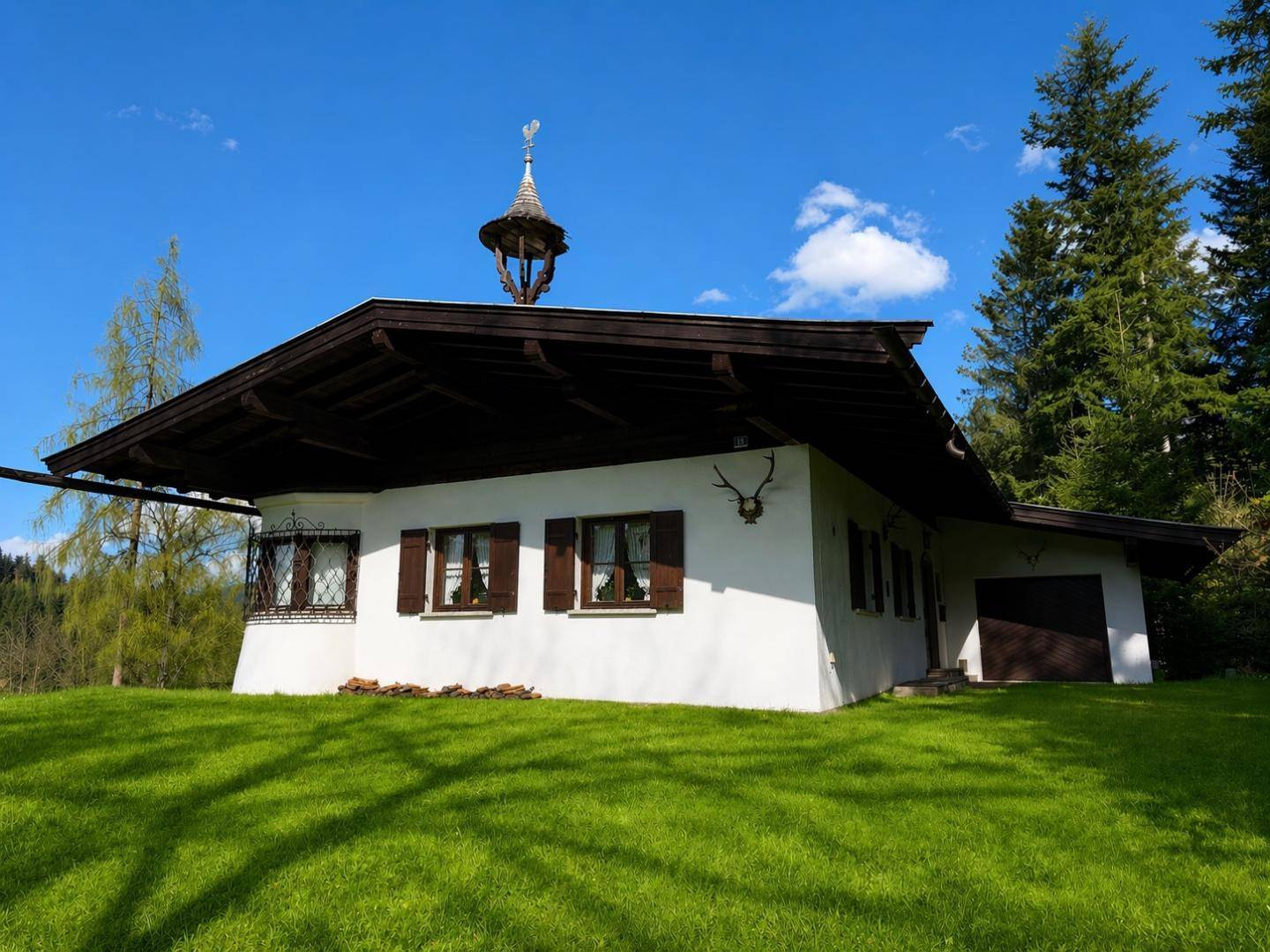 Alpenländisches Haus mit weißer Fassade, Holzfensterläden und einem kleinen Turm auf dem Dach.