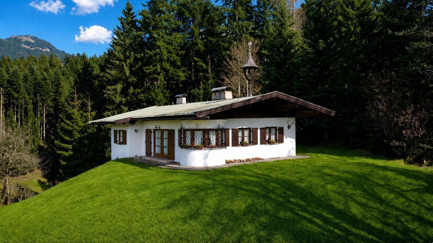 Traditionelles weißes Haus mit Holzelementen, umgeben von Wald und grüner Wiese.