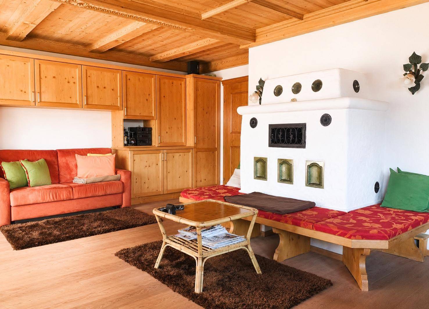 Gemütliches Wohnzimmer im alpinen Stil mit Kachelofen, Holzdecke und bequemen Sitzgelegenheiten.