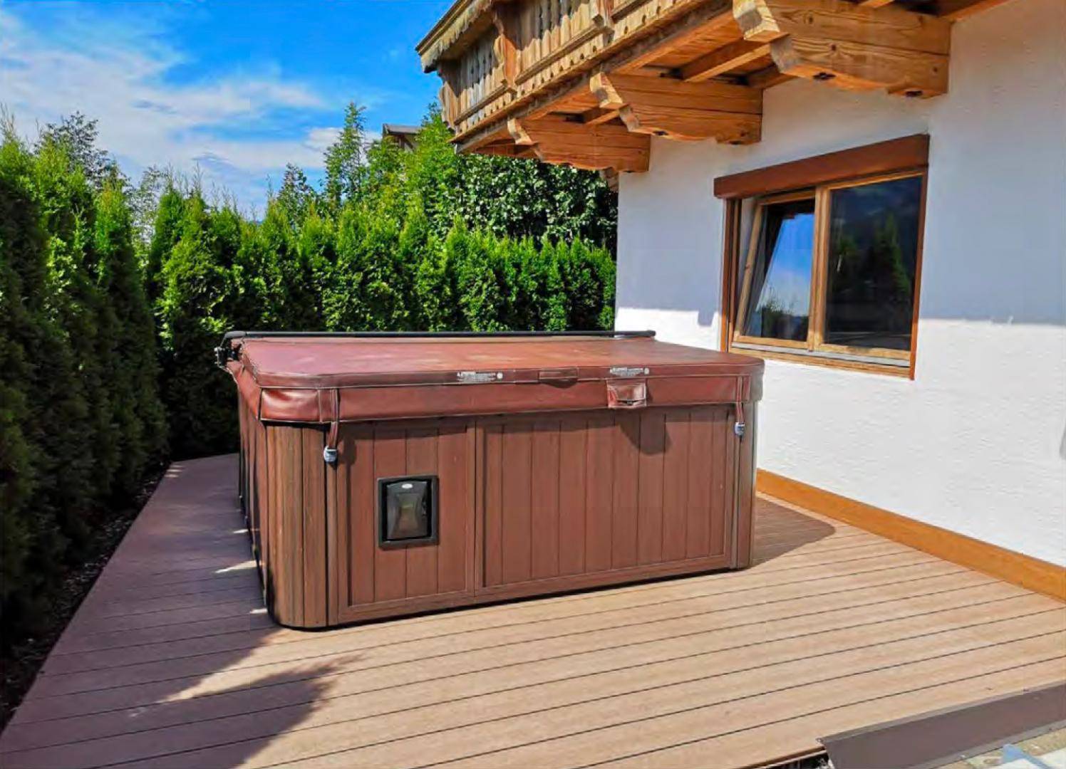 Entspannende Terrasse mit Whirlpool und hohen Hecken für Privatsphäre unter blauem Himmel.