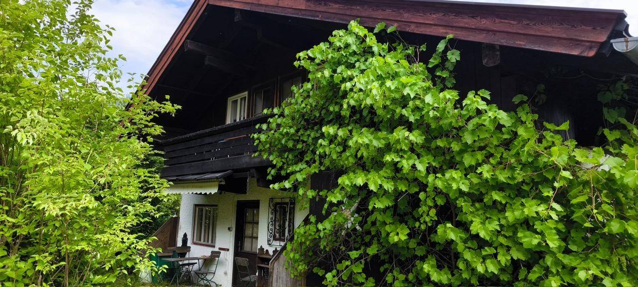 Traditionelles Haus mit Holzbalkon, umgeben von üppigem Grün und Kletterpflanzen.