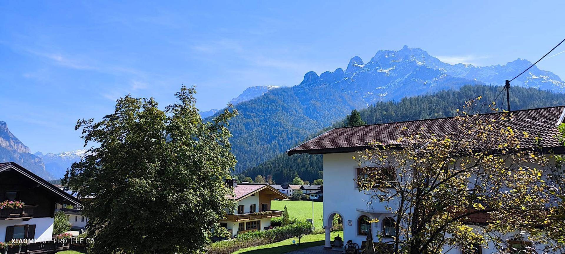 Weitläufiger Blick auf eine beeindruckende Bergkette und traditionelle Häuser in sonniger Umgebung.