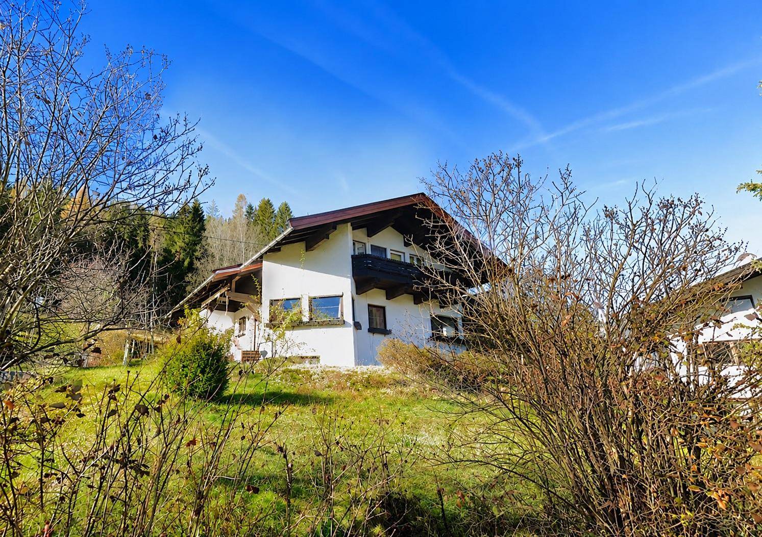 Charmantes weißes Haus im Grünen mit Holzbalkonen und einem gepflegten Gartenbereich.