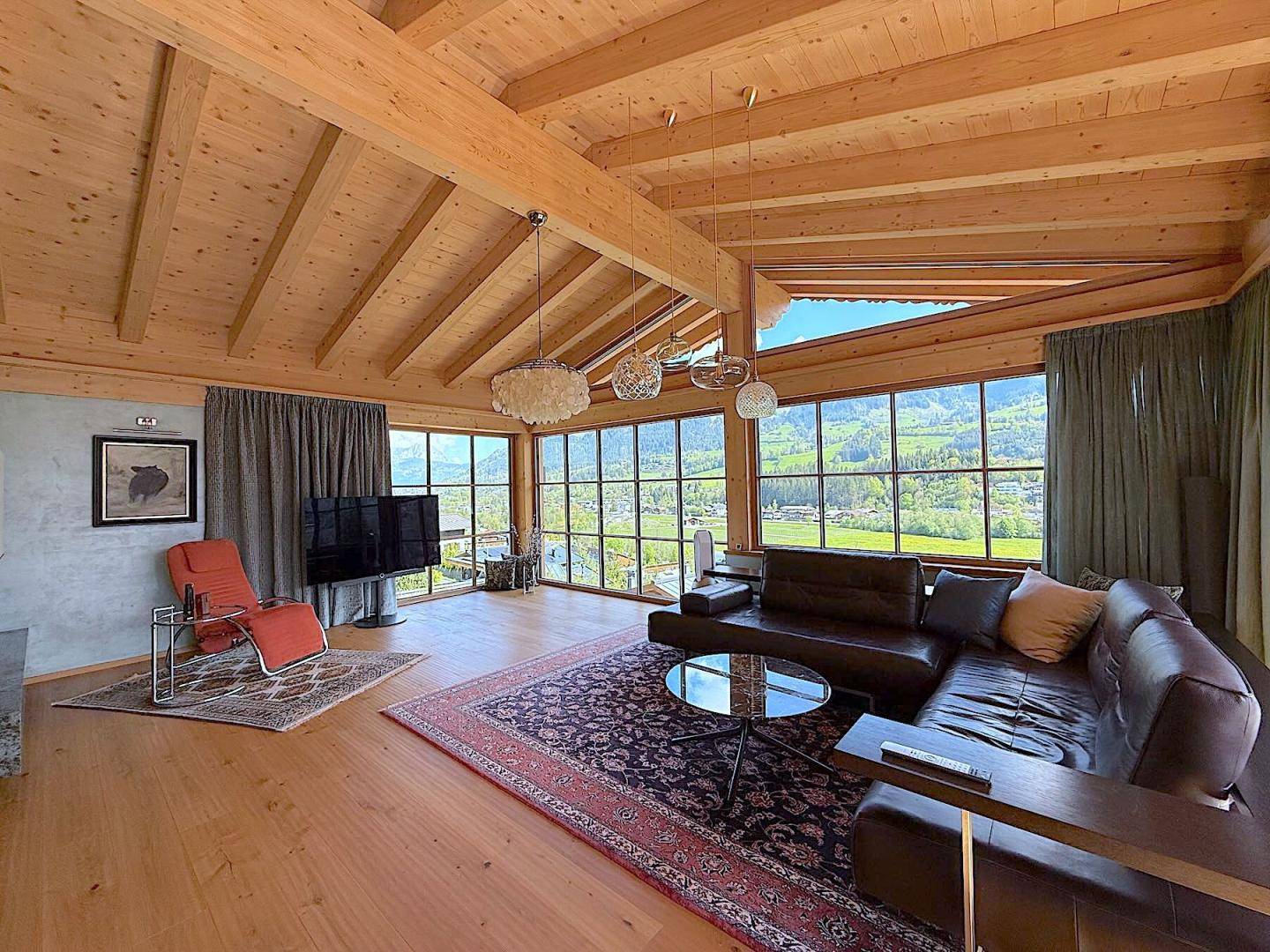 Geräumiges Wohnzimmer mit gemütlicher Sitzecke, Holzboden und weitem Ausblick durch große Fenster.