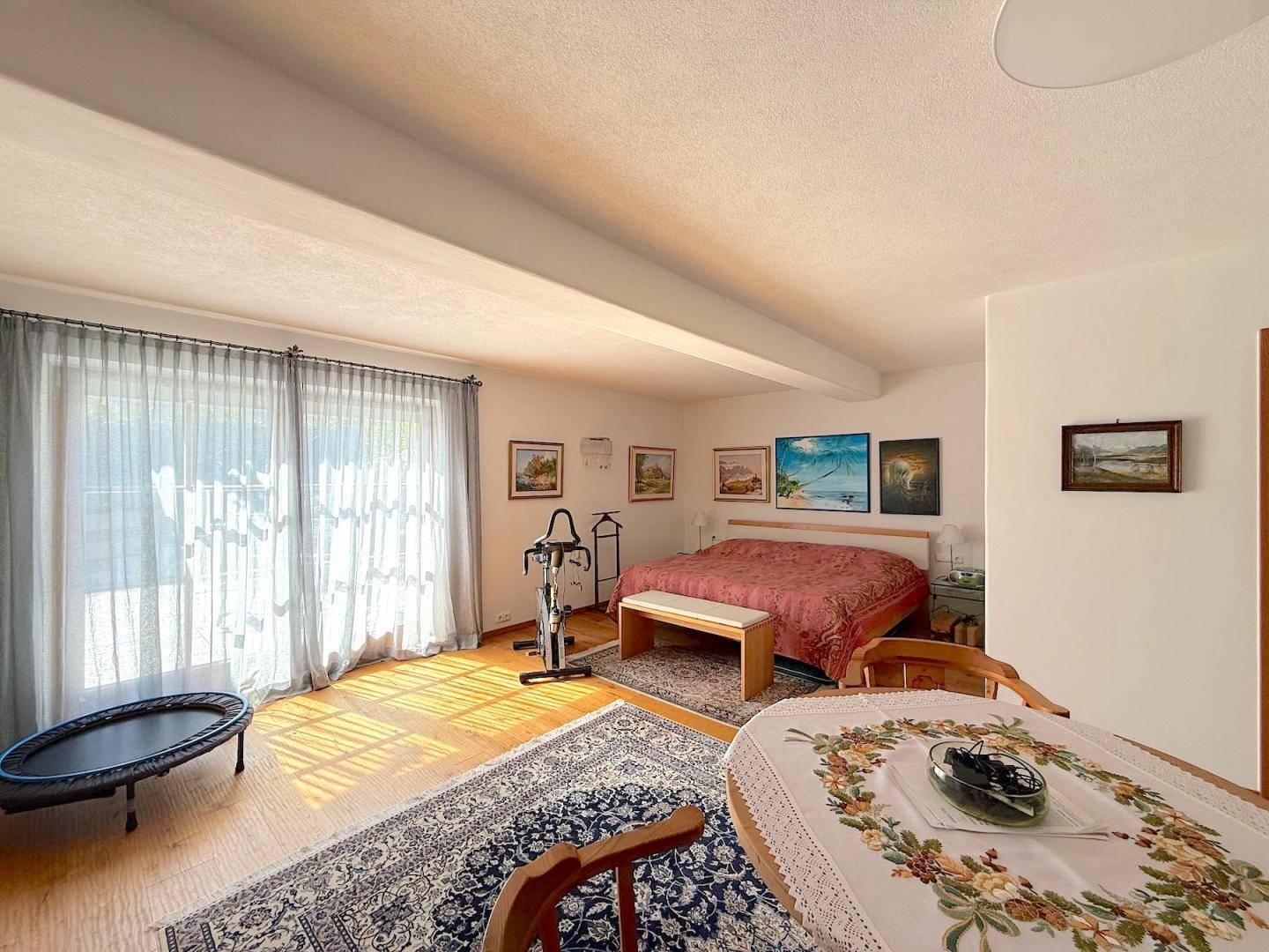 Helles Schlafzimmer mit Holzboden, großem Fenster und einem kleinen Trampolin.
