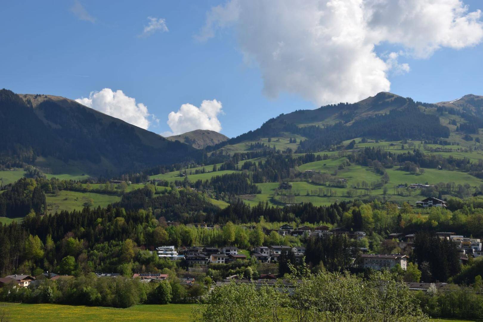 Beeindruckender Ausblick auf die weite Bergwelt mit grünen Wiesen und vereinzelten Häusern.