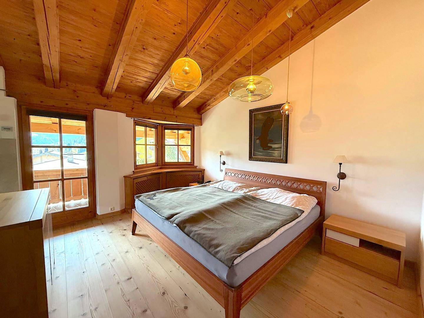 Gemütliches Schlafzimmer mit Holzbalkendecke, Holzboden und Zugang zu einem kleinen Balkon.