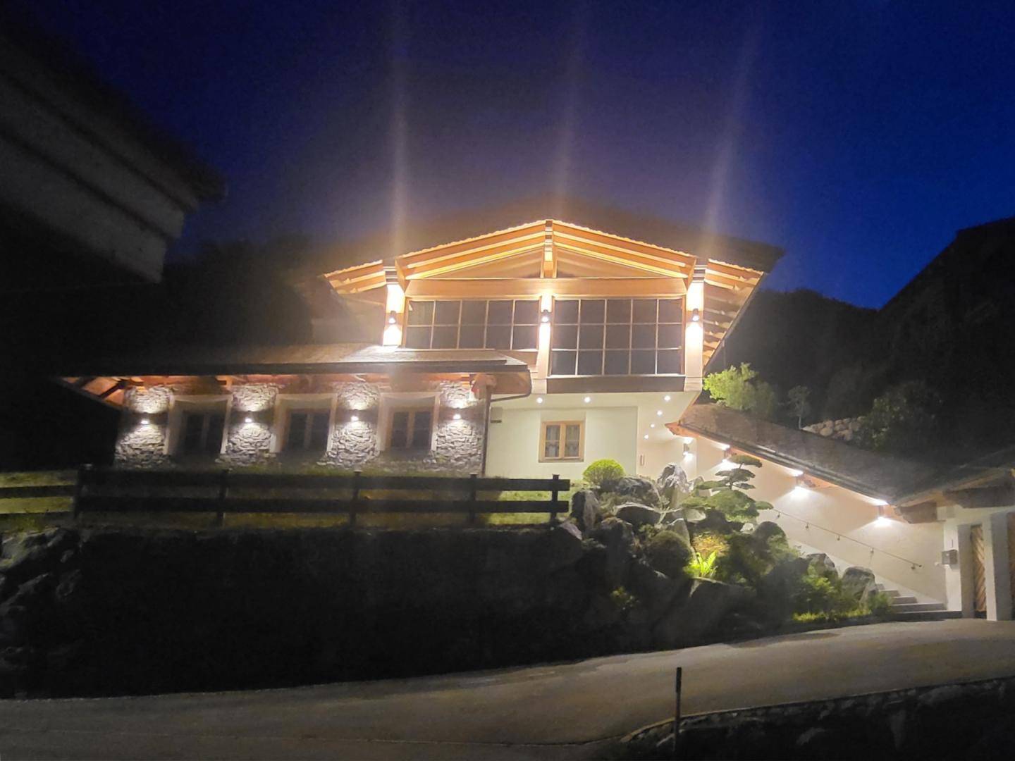Beleuchtetes modernes Chalet bei Nacht, das seine Architektur und die großen Fenster hervorhebt.