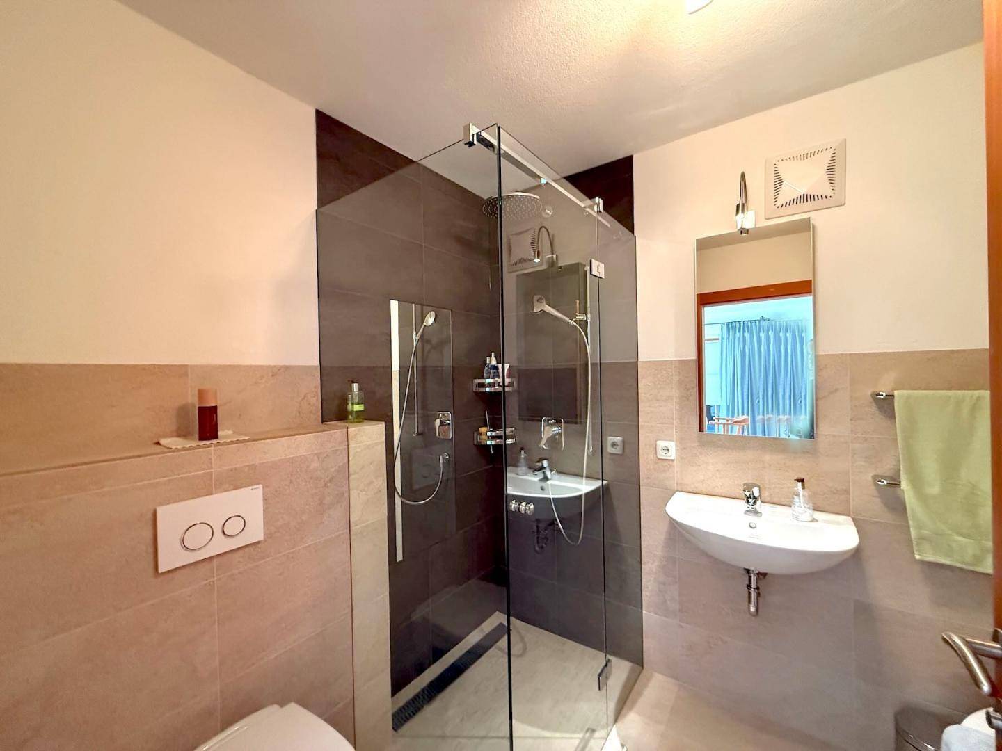 Modernes Badezimmer mit begehbarer Dusche, Waschbecken und Spiegel, in hellen Farbtönen gehalten.