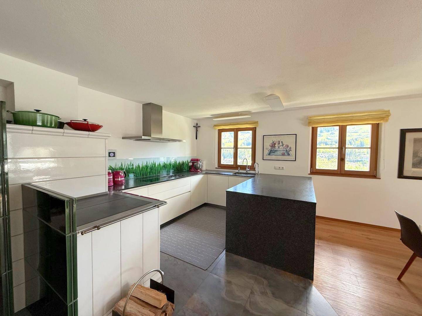 Moderne Küche mit Kochinsel, weißen Fronten und traditionellem Kachelofen, kombiniert mit Holzboden.