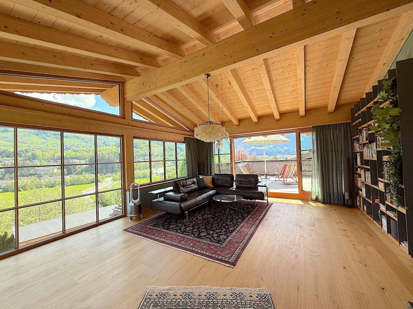Helles Wohnzimmer mit Holzbalkendecke, großen Panoramafenstern und Blick auf die Landschaft.