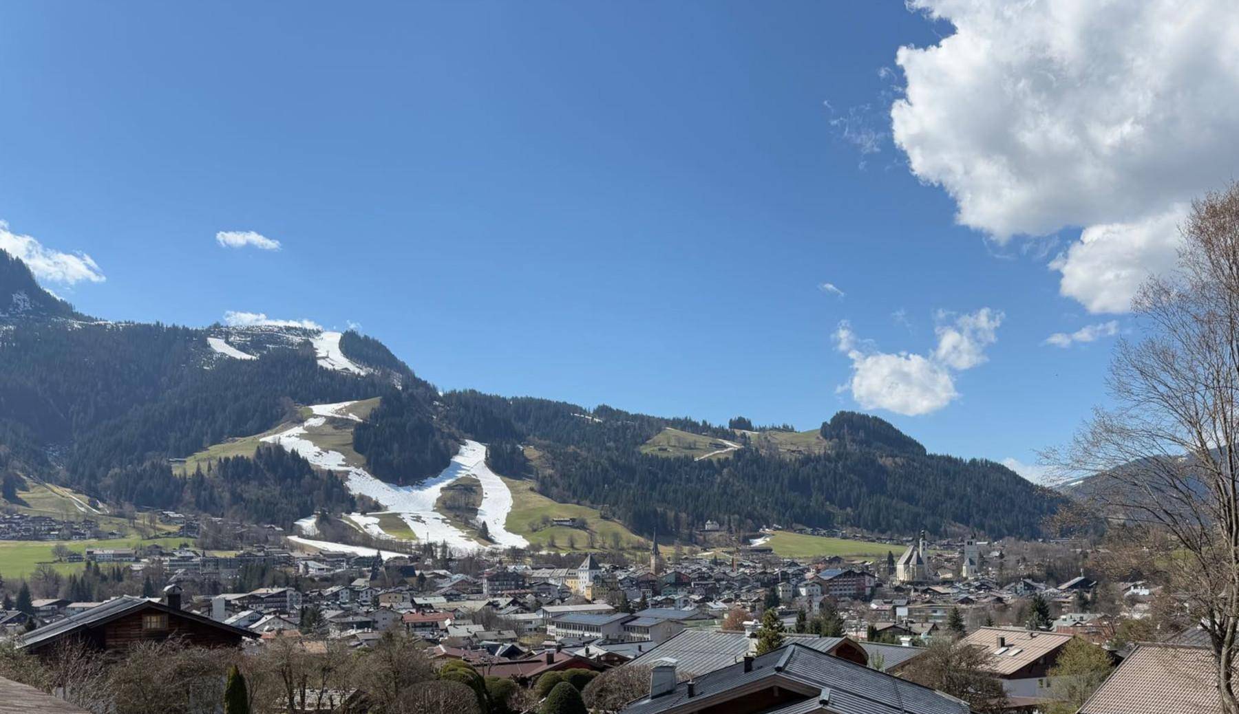 Panoramablick auf eine malerische Stadt im Tal, umgeben von schneebedeckten Bergen und Skipisten.