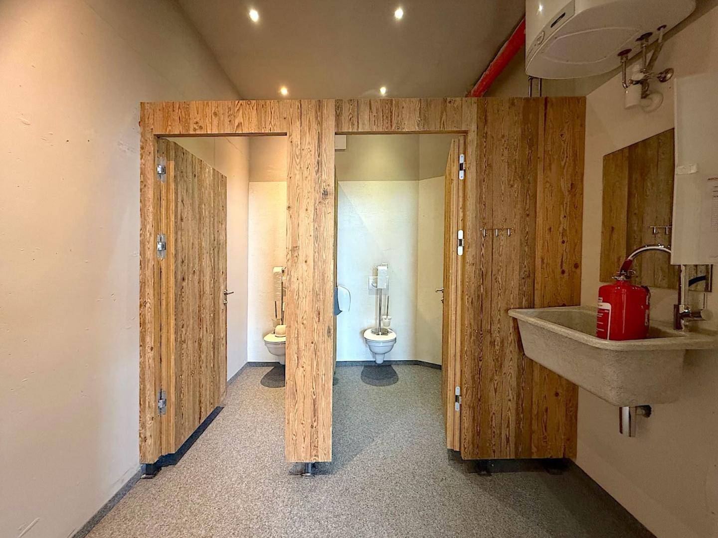 Sauberer Sanitärbereich mit mehreren Toilettenkabinen aus Holz und einem Waschbecken mit Seifenspender.