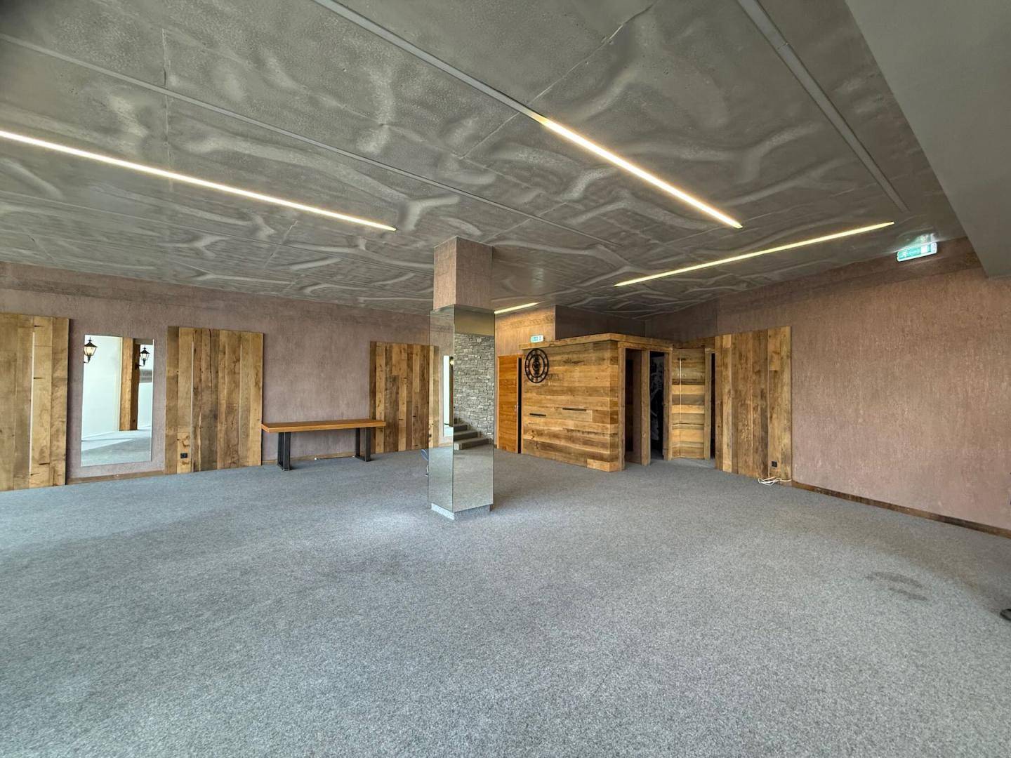 Geräumiger, leerer Innenraum mit grauem Teppichboden, Holzwänden und einem verspiegelten Pfeiler, sehr gepflegt.