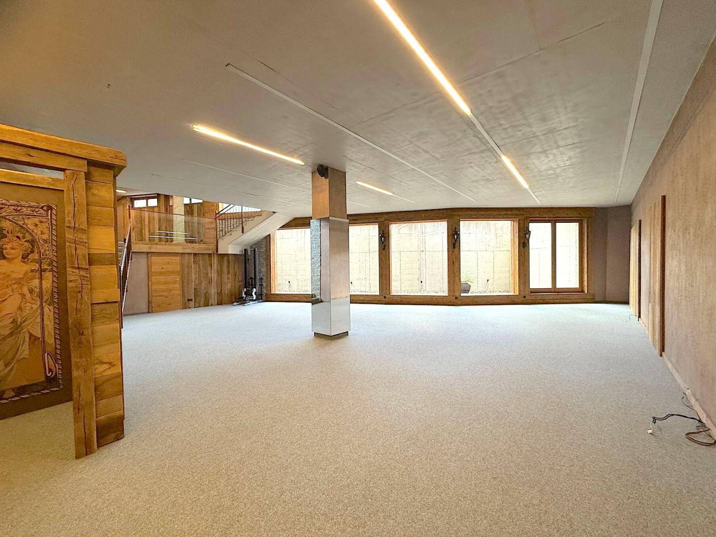 Geräumiger Innenraum mit Teppichboden, Holzelementen und einer Fensterfront, die viel natürliches Licht hereinlässt.