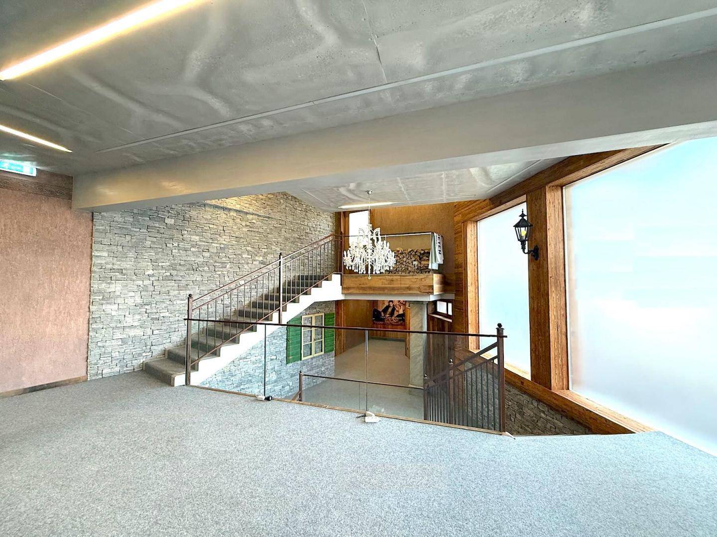Beeindruckendes Treppenhaus mit Steinfassade, Metallgeländer und Blick auf einen unteren Bereich mit Kronleuchter.