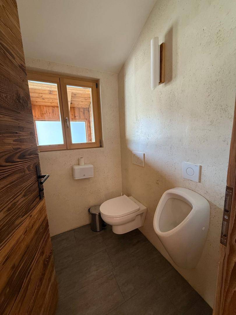Helle Gästetoilette mit Fenster, Urinal und Wand-WC, ausgestattet mit modernen Fliesen.