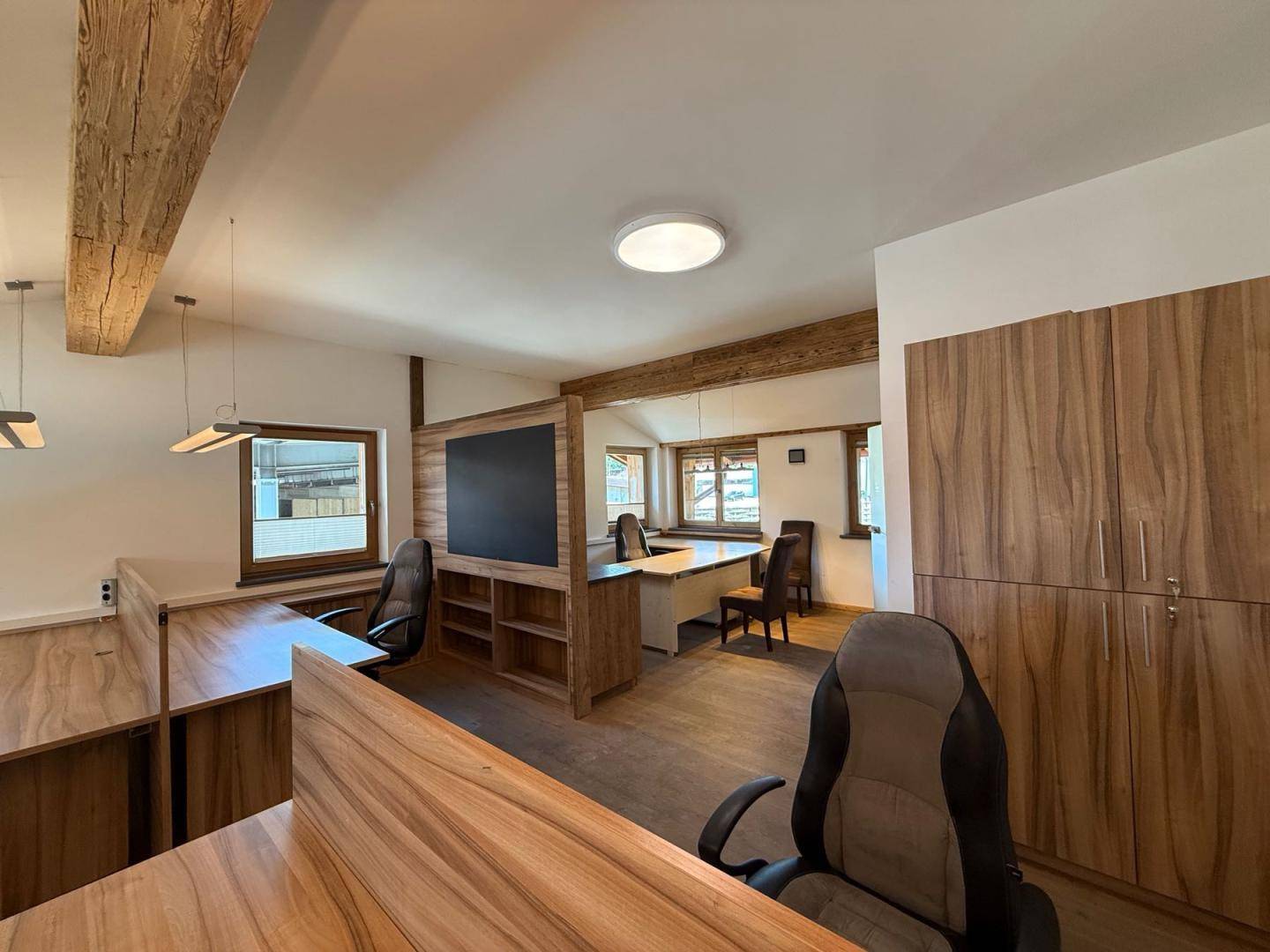 Modern eingerichtetes Büro mit Holztischen, ergonomischen Stühlen und sichtbaren Holzbalken.