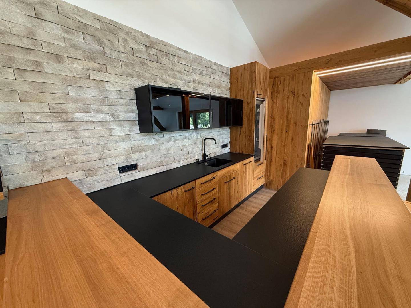 Moderne Holzküche mit schwarzer Arbeitsplatte, Steinwand und integrierten Schränken.