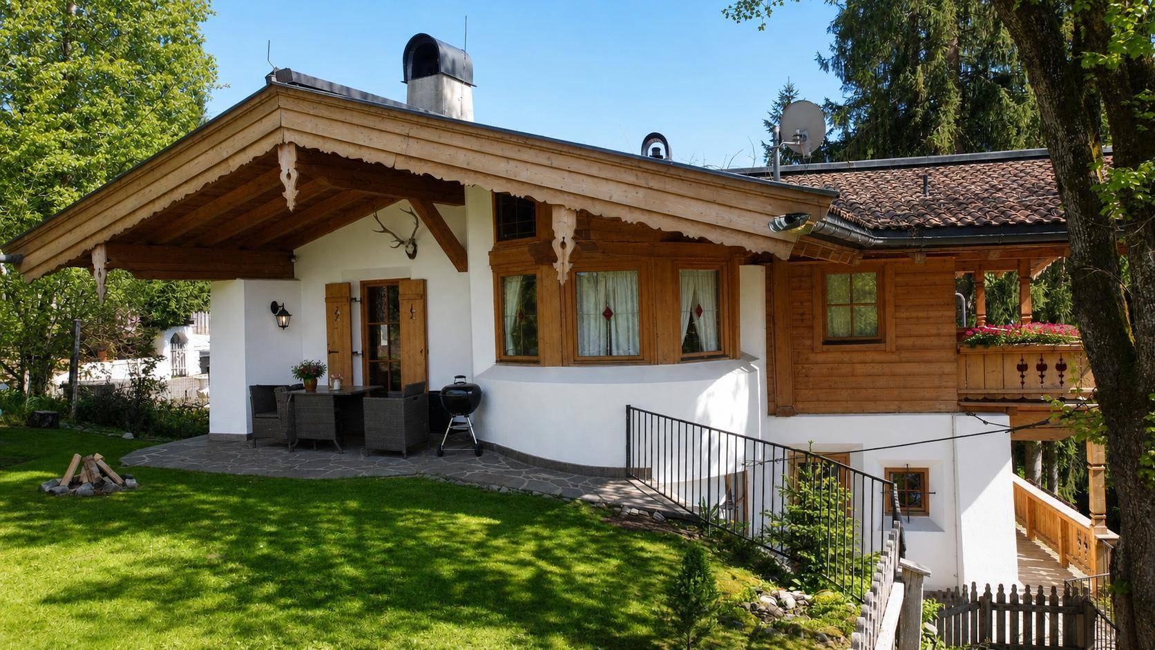 Sonniger Terrassenbereich mit Gartenmöbeln, Grill und Blick auf den gepflegten Rasen.