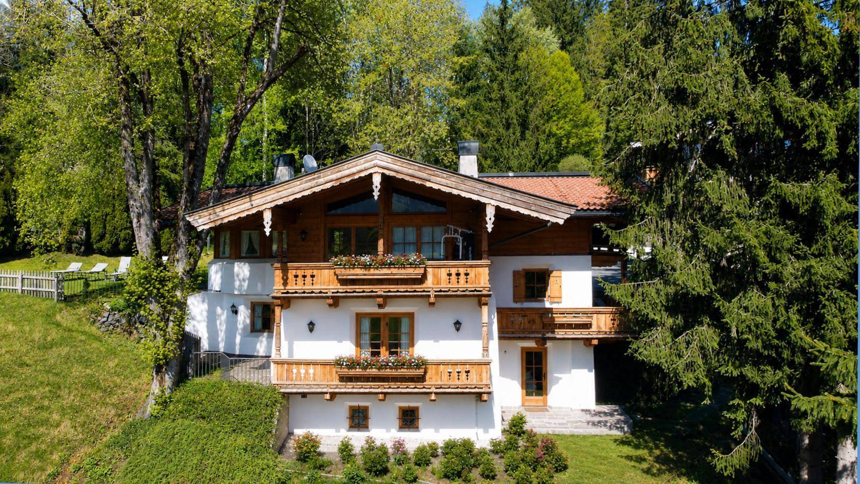 Charmantes Alpenchalet mit weißer Fassade, Holzbalkonen und umgeben von üppiger Natur.
