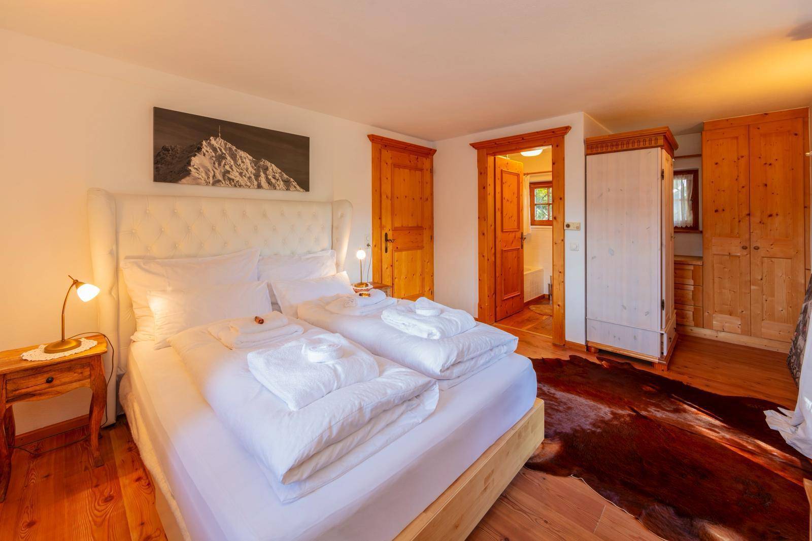 Helles Schlafzimmer mit Doppelbett, Holzschrank und Zugang zu einem weiteren Badezimmer.