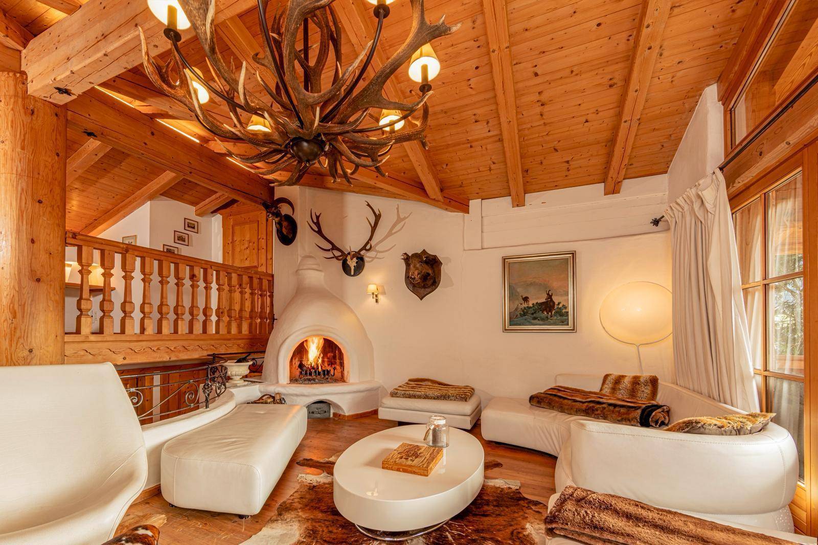 Stilvoller Wohnbereich mit traditionellem Kamin, eleganten weißen Möbeln und Geweih-Kronleuchter.