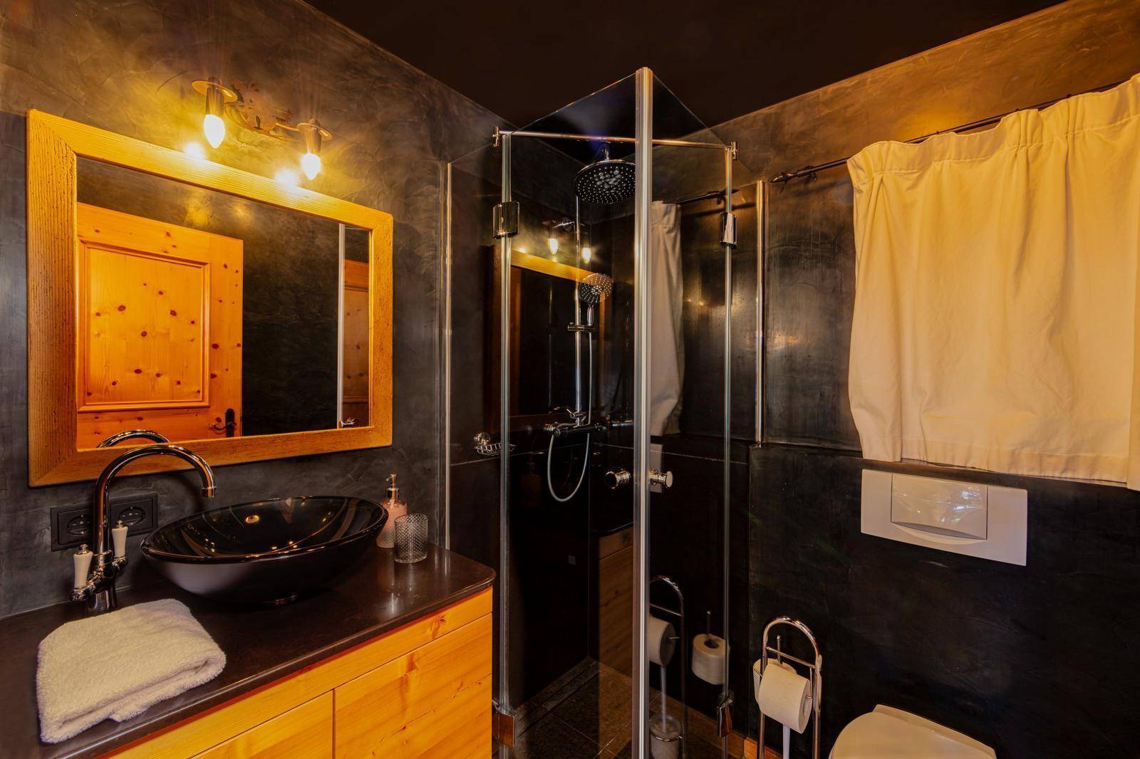 Modernes Badezimmer mit dunklen Wänden, schwarzem Waschbecken und Glasduschkabine.