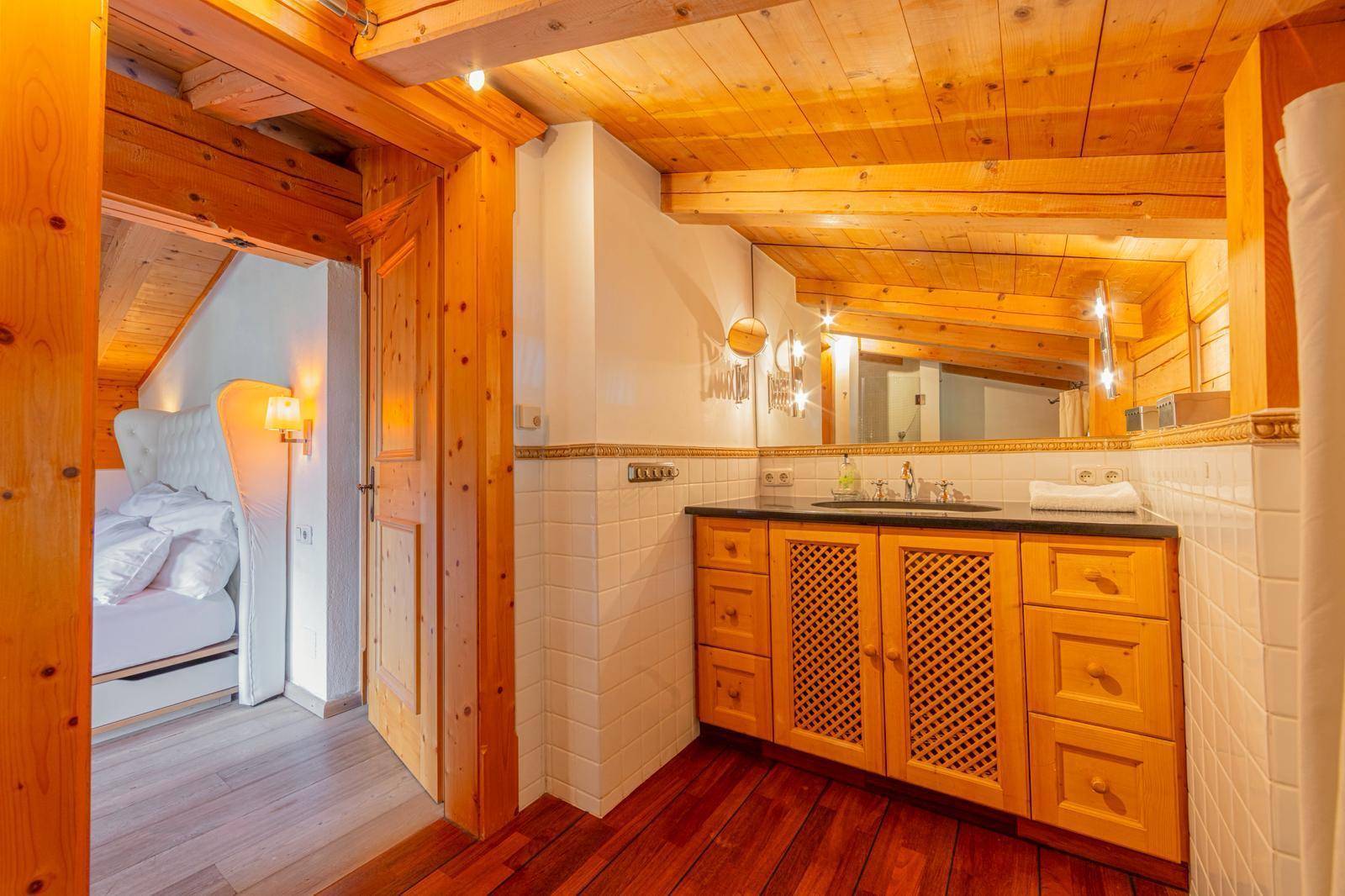 Badezimmer mit Holzwaschtisch, Spiegel und sichtbaren Holzbalken an der Decke.