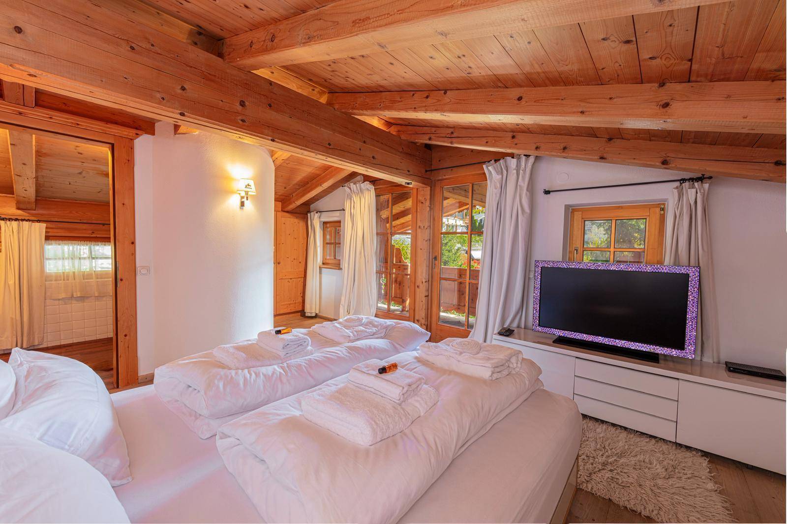 Helles Schlafzimmer mit Holzbalkendecke, Fernseher und Zugang zu einem Balkon.