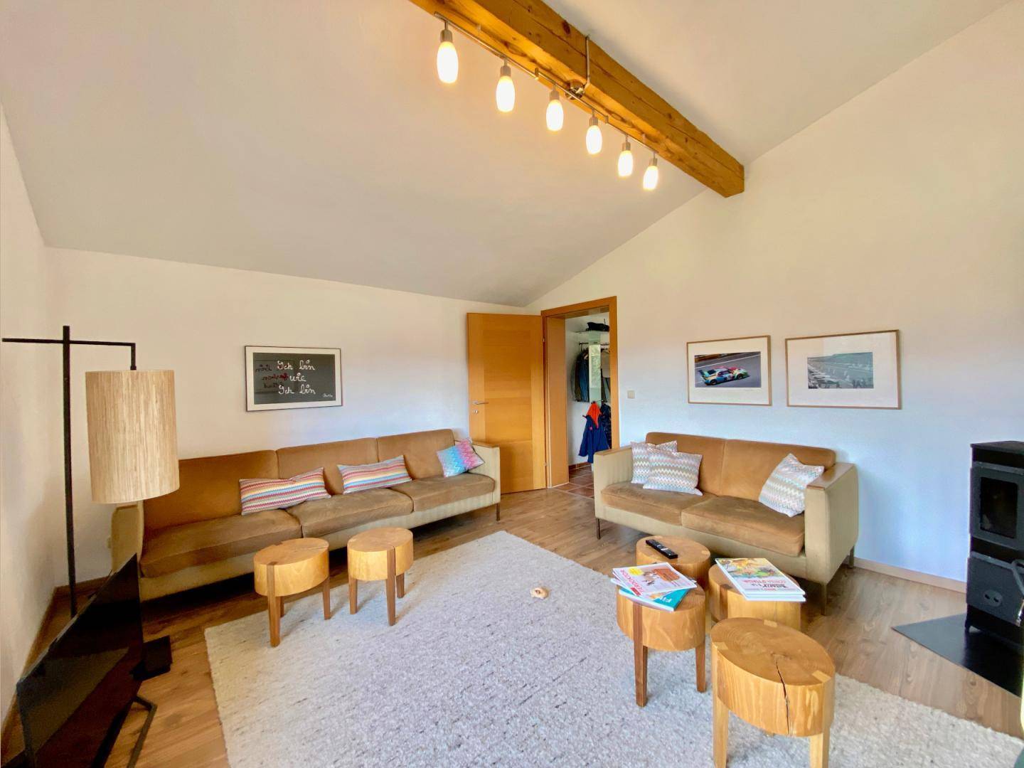 Helles Wohnzimmer mit Holzbalken, gemütlichen Sofas und modernem Kaminofen.