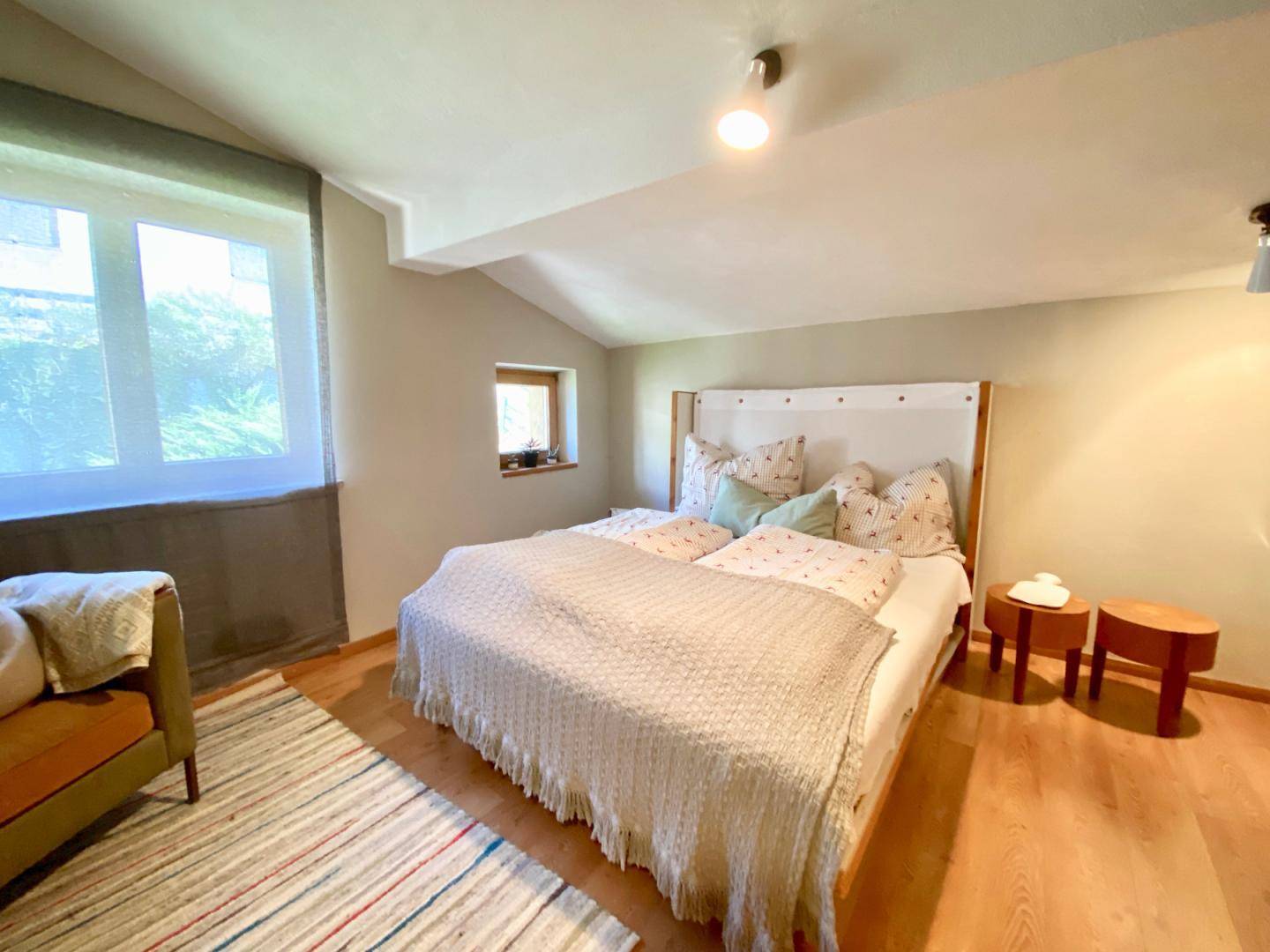 Gemütliches Schlafzimmer mit Holzboden, schrägen Decken und großen Fenstern.