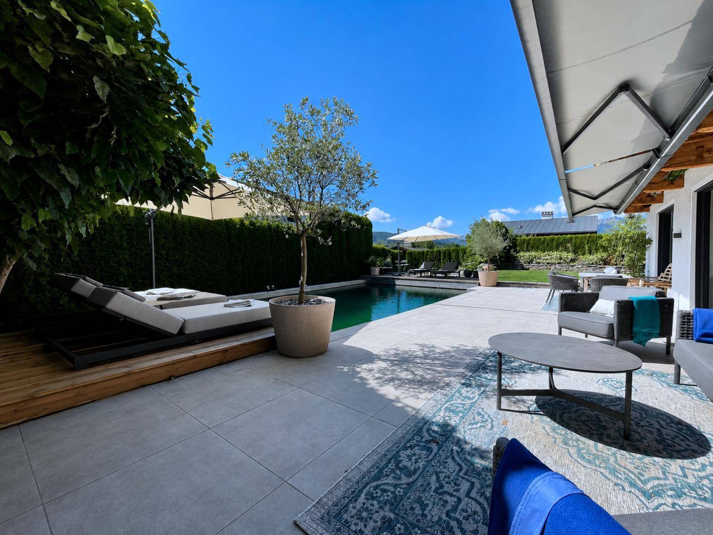 Großzügige Terrasse mit Swimmingpool, bequemen Lounge-Möbeln und Sonnenschutz unter blauem Himmel.