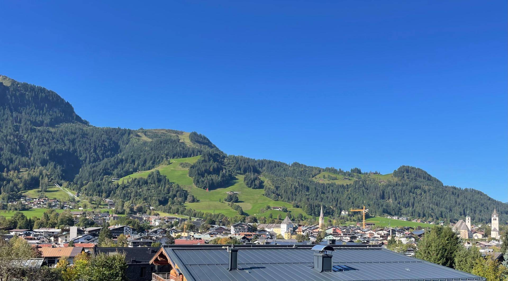 Weitläufige grüne Berglandschaft mit einem malerischen Dorf im Tal unter blauem Himmel.